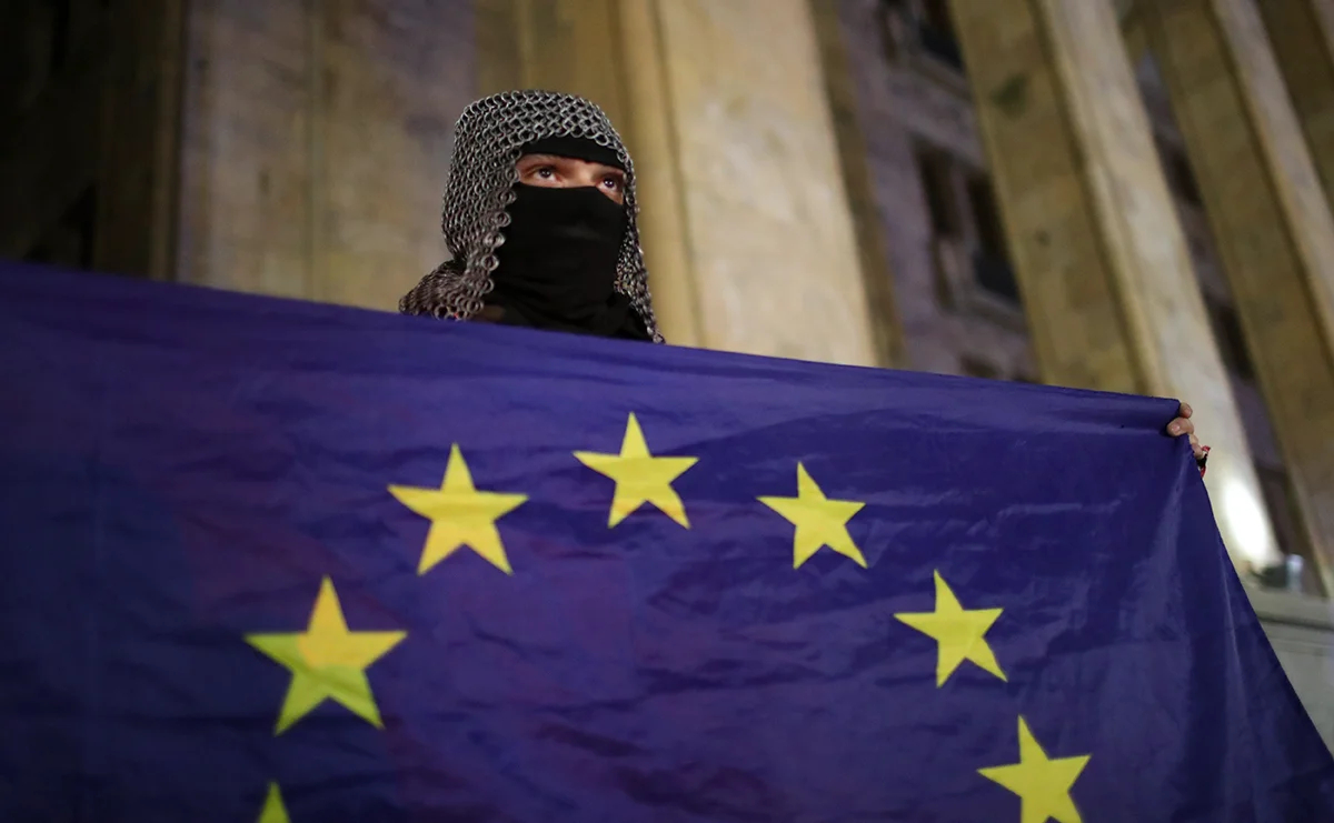 Сторонник грузинской оппозиции держит флаг ЕС во время акции протеста перед зданием парламента в Тбилиси, Грузия, 6 декабря 2024 года. Фото: David Mdzinarishvili / EPA
