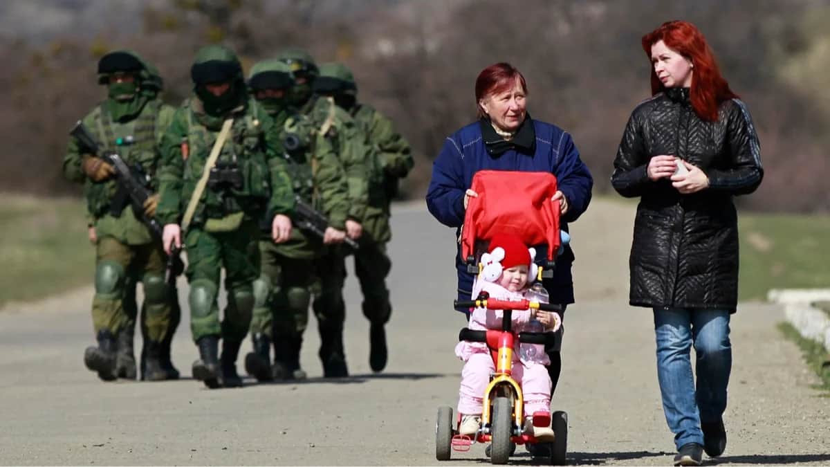 Местные жительницы проходят мимо вооруженных людей в военной форме без опознавательных знаков у входа в украинскую воинскую часть в селе Перевальное под Симферополем, 14 марта 2014 года. Фото: Юрий Кочетков / EPA